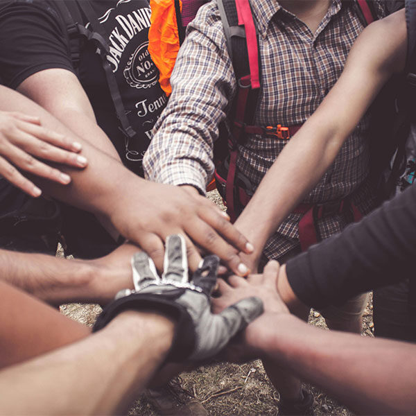 EN: A group of people forming a circle, their hands joined at the center in a gesture of unity. FR: Un groupe de personnes formant un cercle, leurs mains jointes au centre dans un geste d’unité.